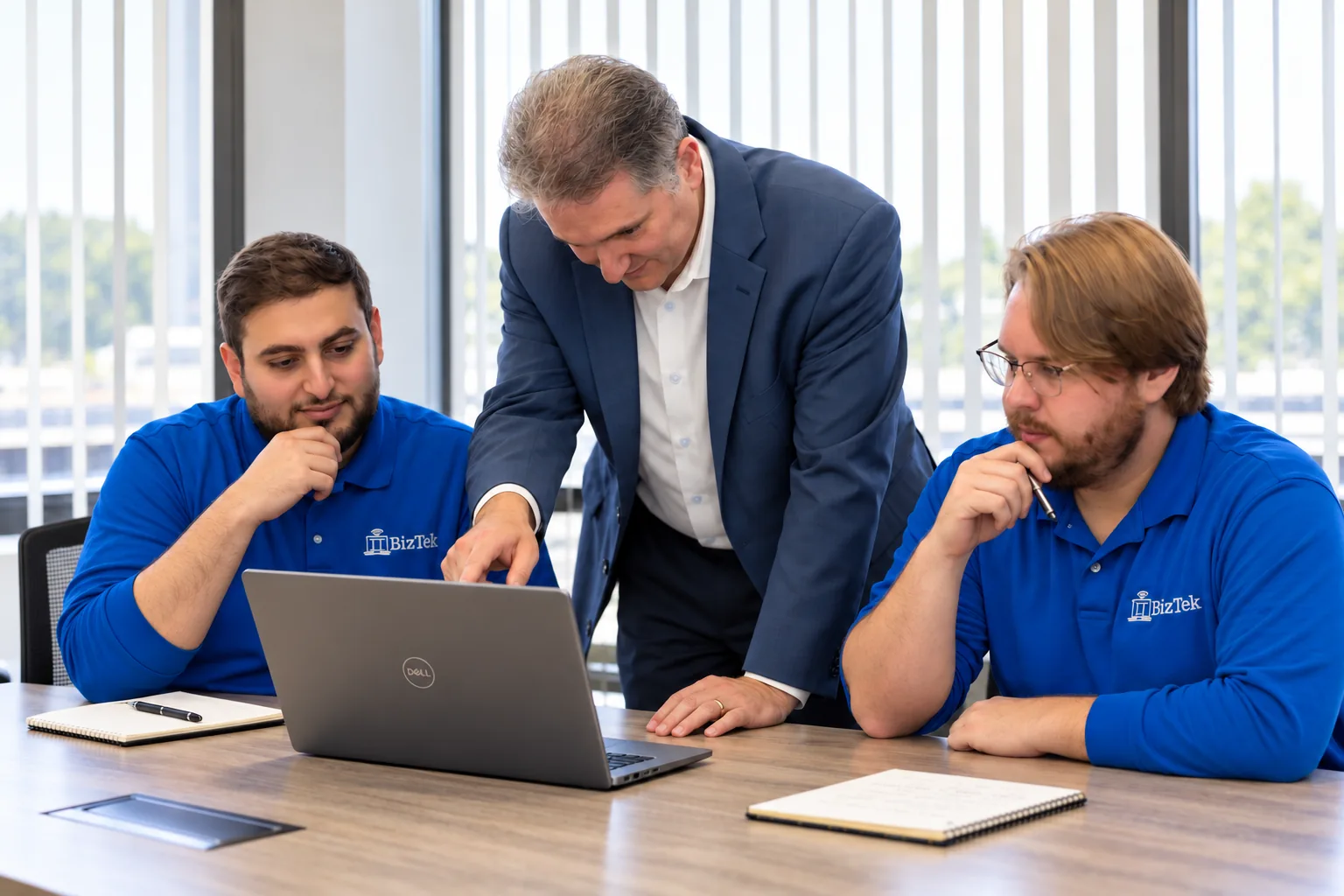 Three ITBizTek team members discussing a laptop at a meeting table.